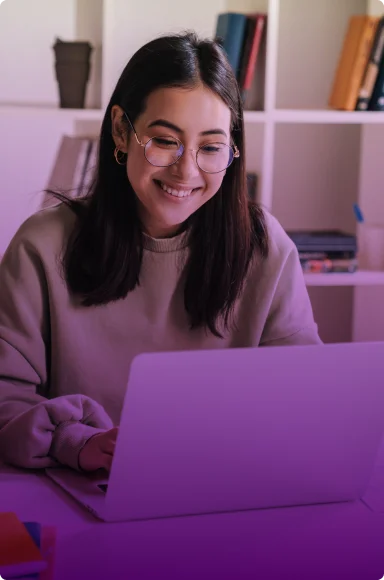 A woman wearing glasses smiles while using a laptop.